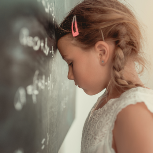Girl leans head against chalkboard, sad.