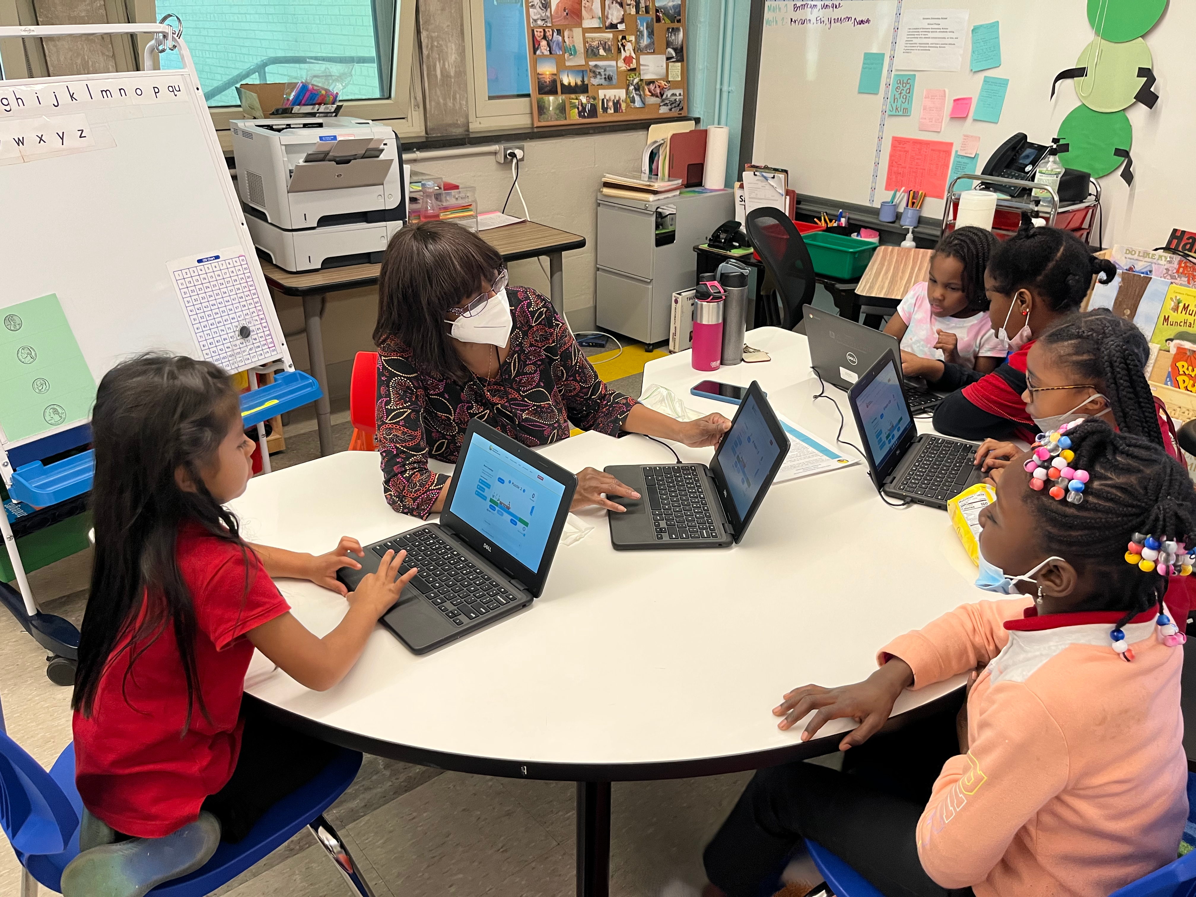 A group of students and a teacher play a math game on their laptops